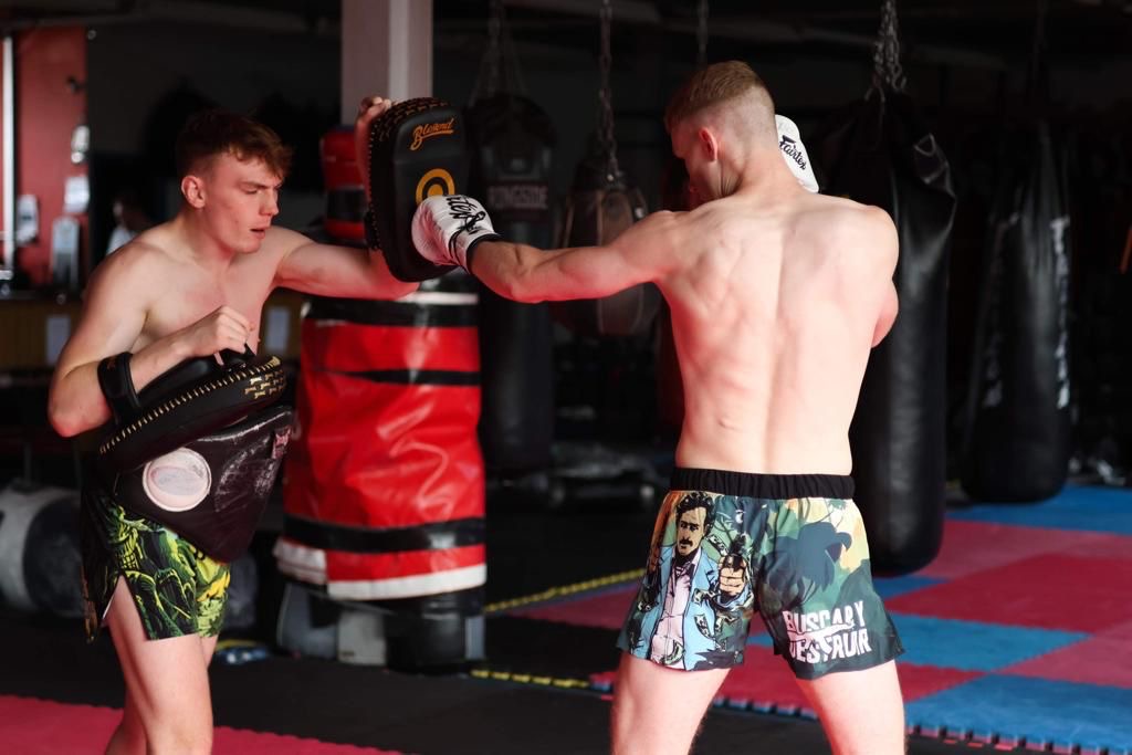 Fighter in BFAST shorts throwing a punch at a pad held by a training partner in a gym